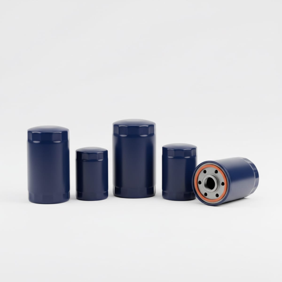 A row of five plain navy oil filter canisters of different heights, with one tipped on its side to show the threaded base plate and orange gasket